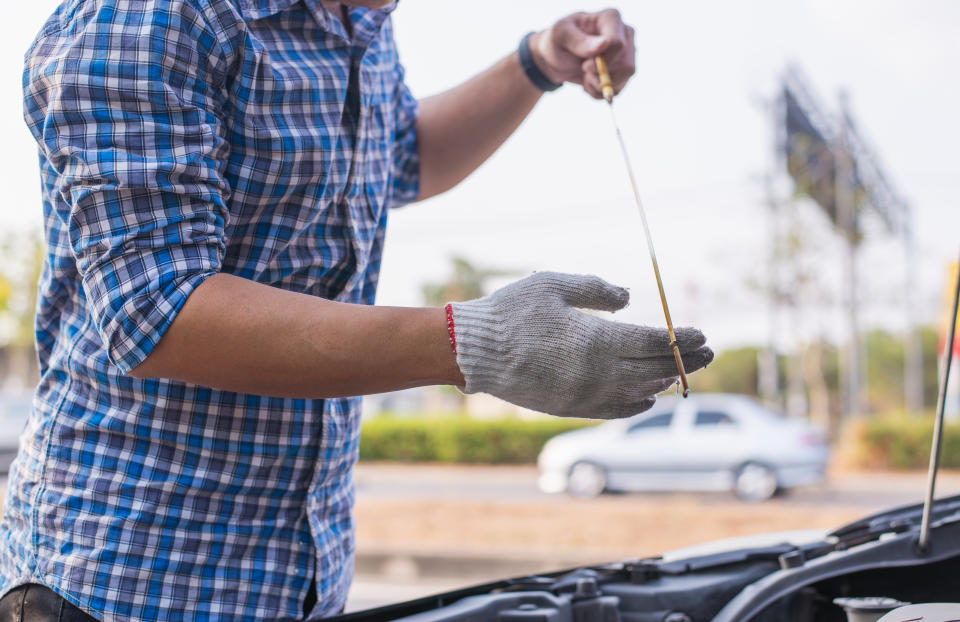 A person wearing a plaid shirt and gloves is checking the oil level of a car's engine with a dipstick