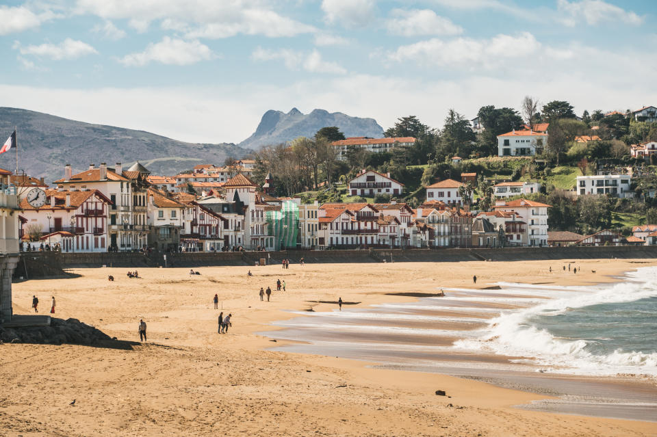 Beach with people and traditional houses on a hill under a clear sky