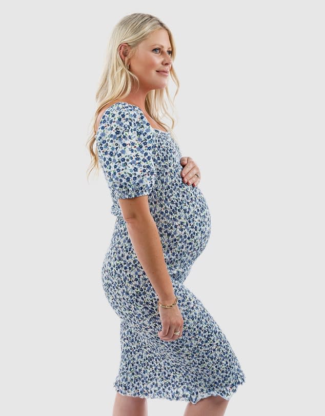 A pregnant woman with long blonde hair wears a blue flowered Confetti Shirred Maternity Dress, $94.95, Maive & Bo 