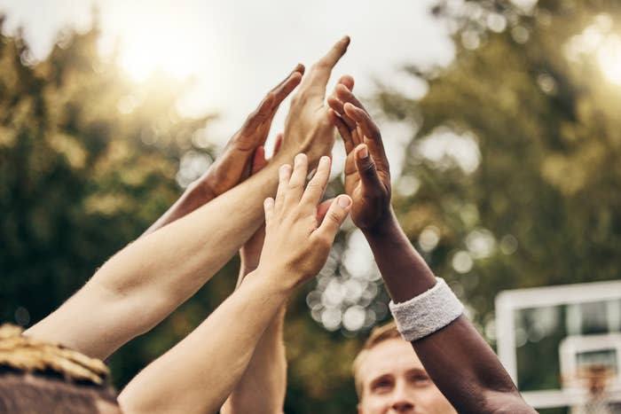 Hands of several people reach up, united in a high-five gesture, outdoors in a positive and collaborative spirit