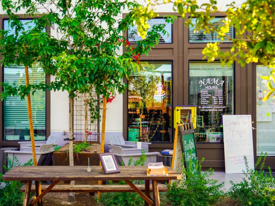 Culdesac Tempe: A shop with brown doors behind an outdoor table, trees, and shrubbery