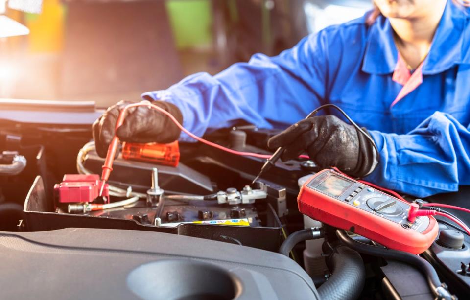 An electrician in a blue suit uses a tool to assess an electrical system.