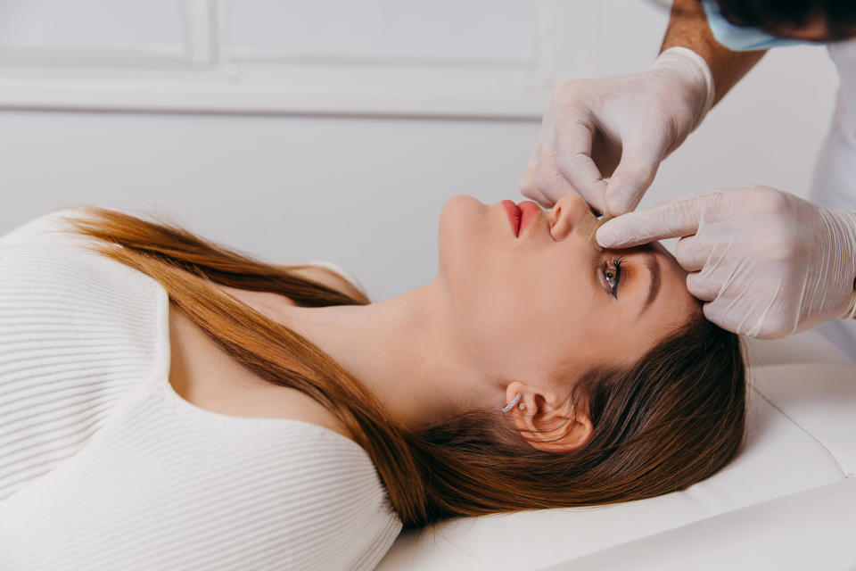 A doctor inspects a woman's nose after a rhinoplasty procedure