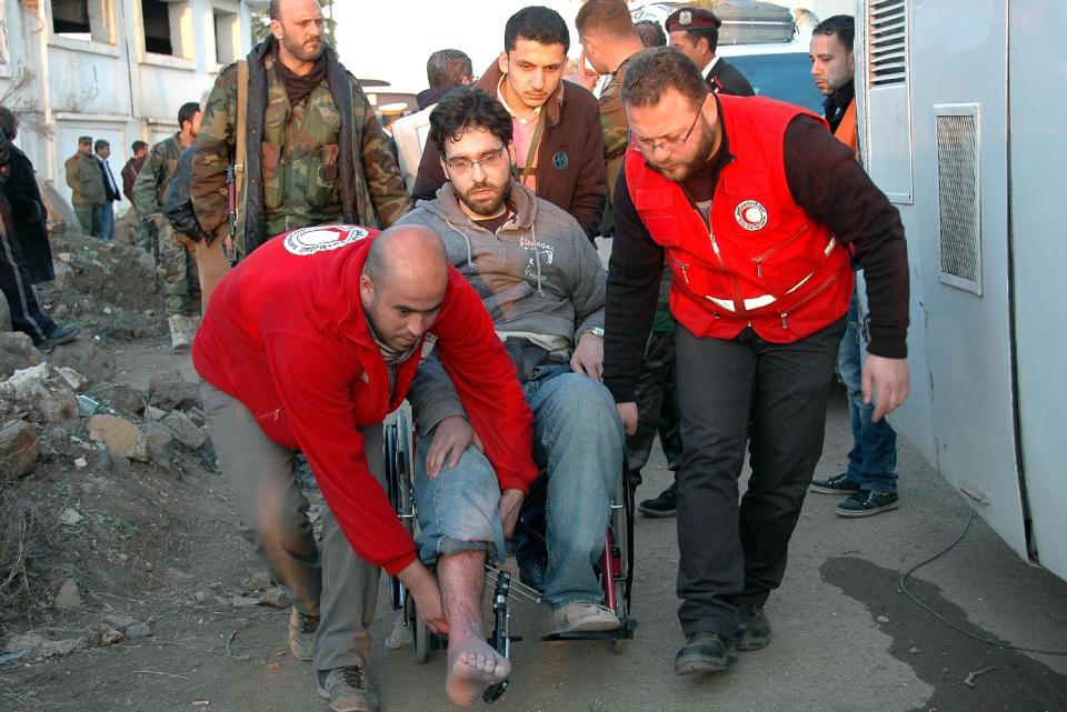 In this Sunday, Feb. 9, 2014 file photo, released by the Syrian official news agency SANA, Syrian Arab Red Crescent members, in red uniforms, help evacuate an injured man to a bus out of the battleground city of Homs, Syria. Weeping children begged for food in the streets and women picked grass growing in the cracks of the sidewalks to eat as hunger gripped residents of rebel-held neighborhoods of the Syrian city of Homs blockaded for nearly two years by the military, according to a rare first-hand account by a man evacuated during a truce this week. (AP Photo/SANA, File)