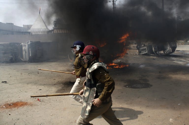 Indian police run past burning cars during a trade union strike in Nodia on the outskirts of New Delhi on February 20, 2013. Protests over the economy turned ugly in Noida, a sprawling suburb of New Delhi, when a mob threw stones and set vehicles on fire before police brought the situation under control