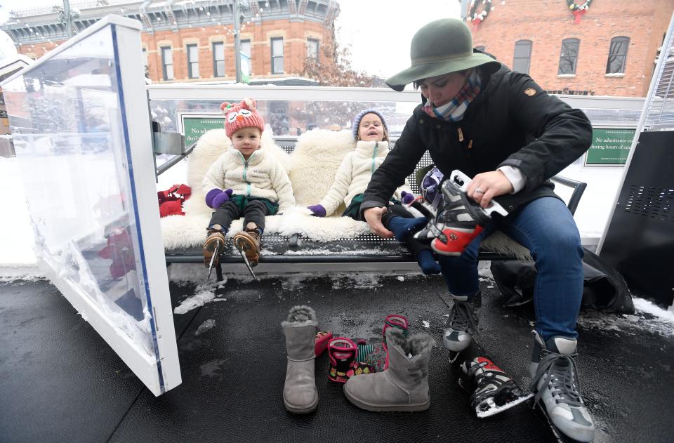 Katie Meadows takes a skate off her daughter Madeleine Usher, 4, as her other daughter Willow Usher, 3, waits next to the ice rink at Old Town Square in Fort Collins, Colo. on Wednesday, Nov. 27, 2019. 