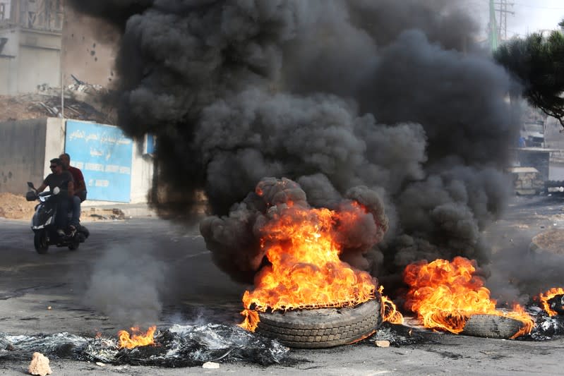 Men ride a motorbike past burning tires blocking a street during a protest targeting the government over an economic crisis, in Nabatiyeh