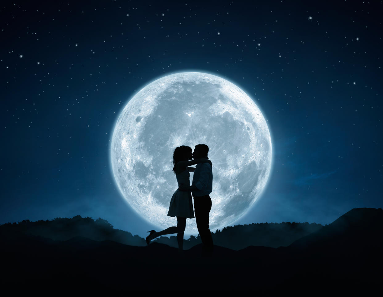 Silhouette of loving couple kissing against the full moon 