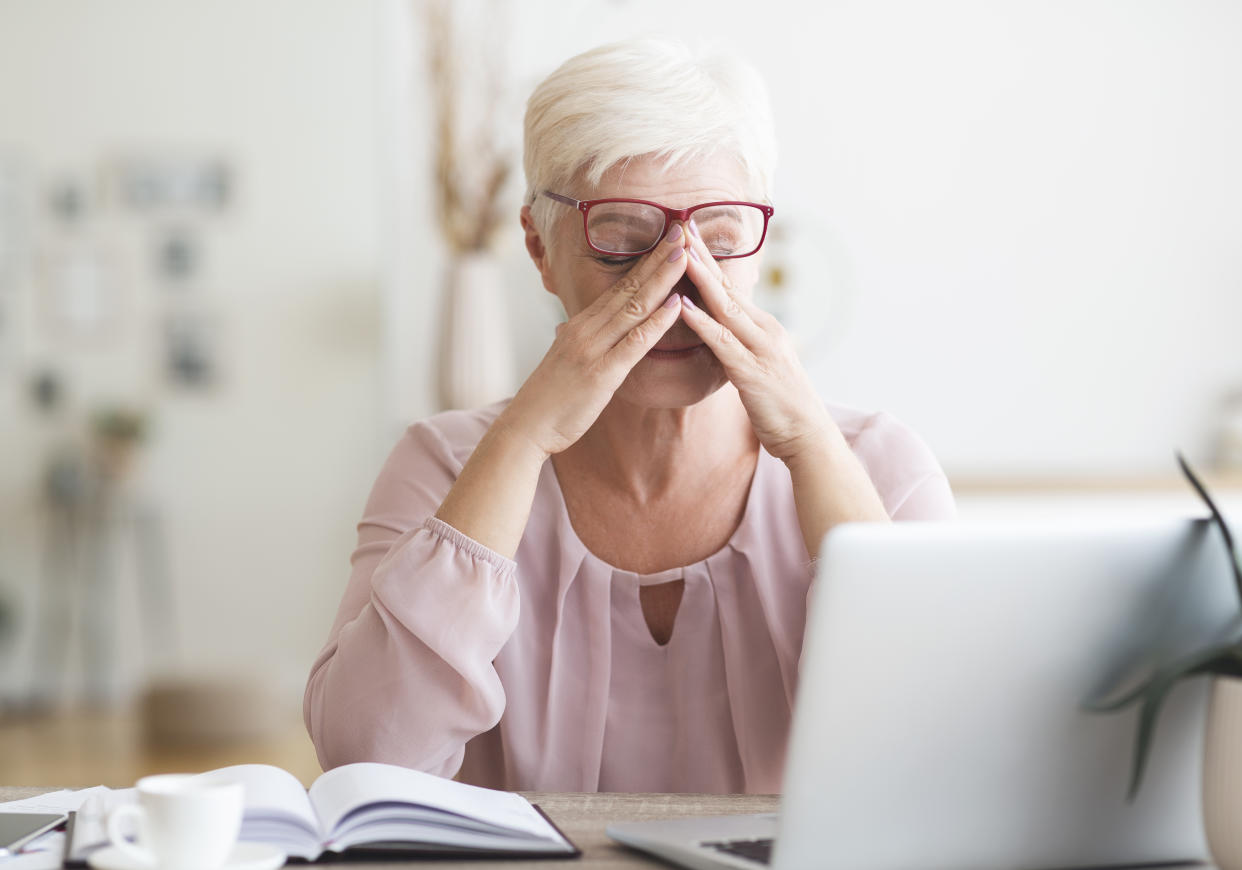 Senior tired business woman overworking in front of laptop, touching her eyes, free space