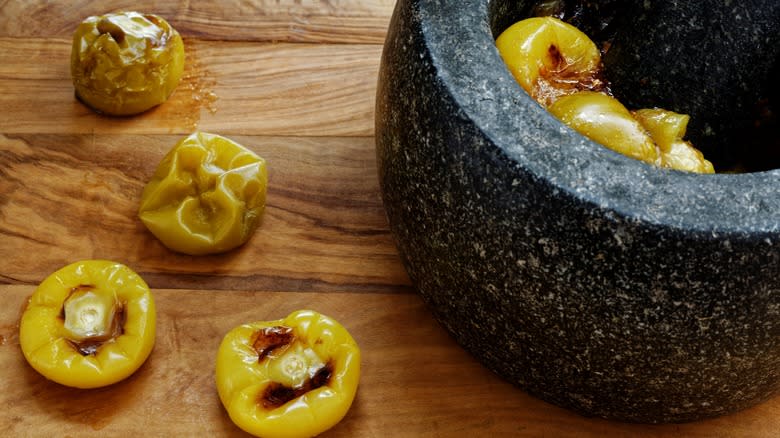 roasted tomatillos on a cutting board and in a traditional molcajete