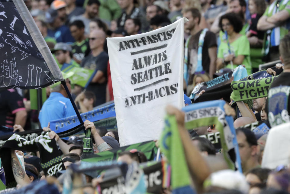 In this July 21, 2019, photo, a sign that reads "Anti-Facist Always Seattle Anti-Racist" is displayed in the supporters section during an MLS soccer match between the Seattle Sounders and the Portland Timbers in Seattle. Major League Soccer's new policy that bans political displays at matches is drawing attention in the Pacific Northwest, where supporters' culture is often intertwined with politics and social issues. (AP Photo/Ted S. Warren)