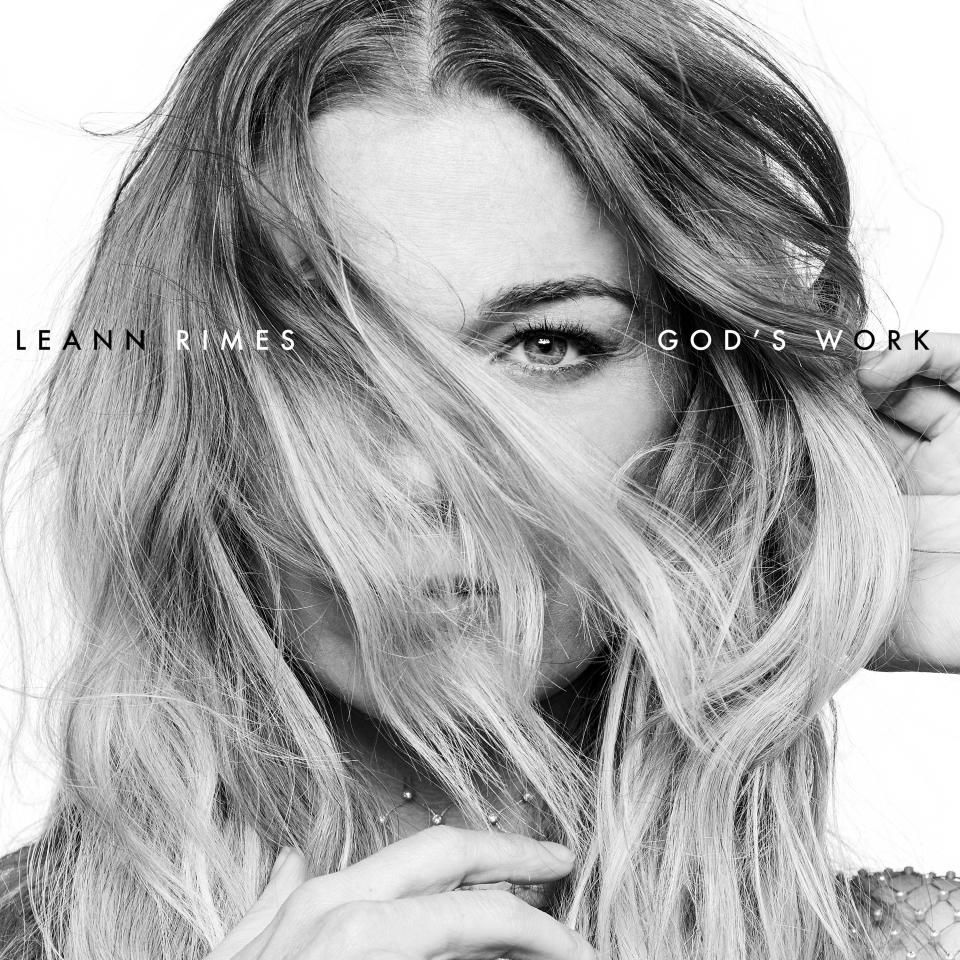 A black and white album cover featuring a close-up of LeAnn Rimes with part of her face covered by her hair. The cover includes the titles of the album, "GOD'S WORK."