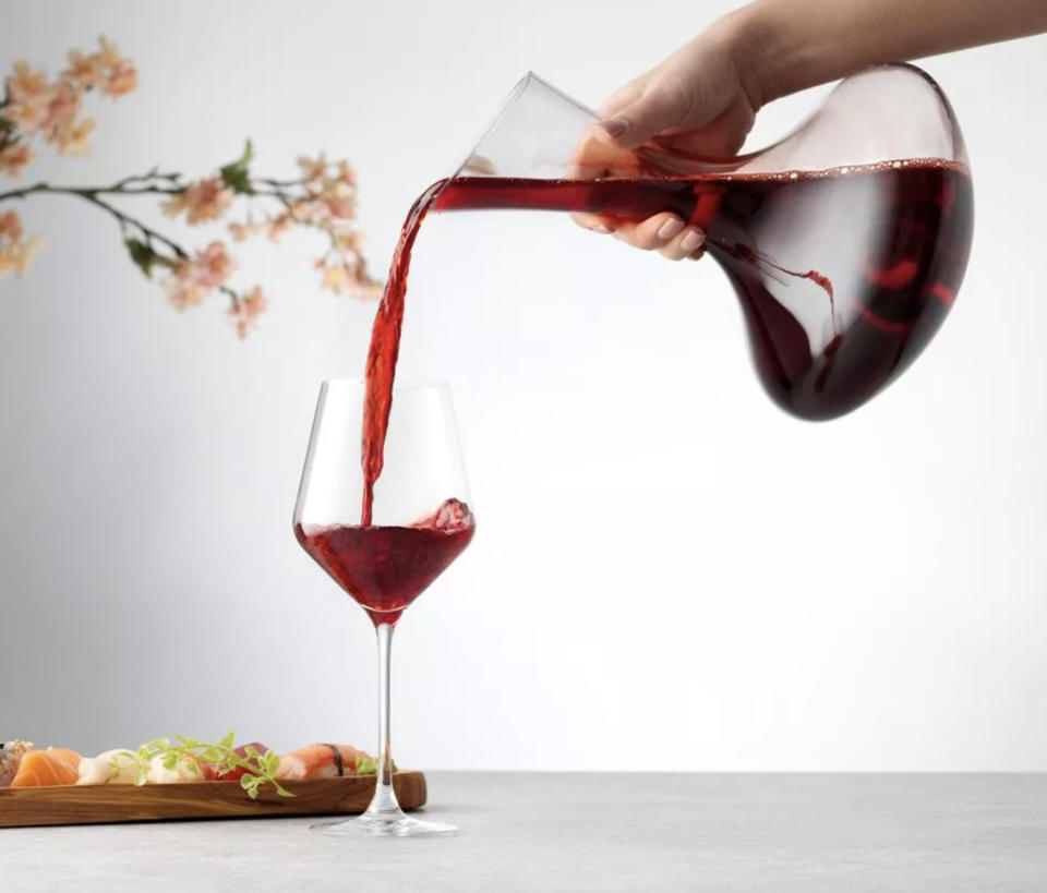 model pouring decanter filled with red wine into glass