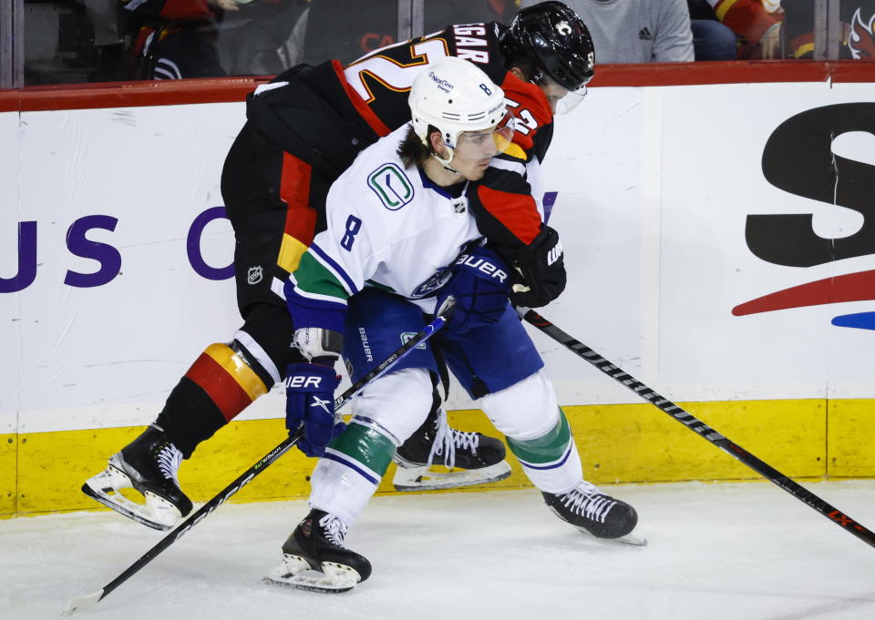 Vancouver Canucks forward Conor Garland, left, checks Calgary Flames defenseman MacKenzie Weegar during the second period of an NHL hockey game in Calgary, Alberta on Wednesday, Dec. 14, 2022. (Jeff McIntosh/The Canadian Press via AP)