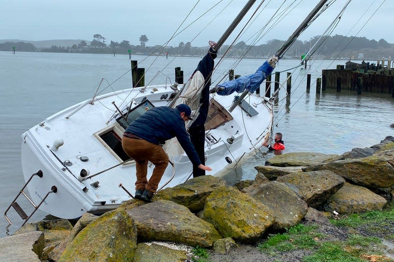 Two men tend to a sailboat that broke anchor at Porto Bodega and wound up on the rocks during a storm in Bodega Bay, California, Thursday, Jan. 5, 2023.
