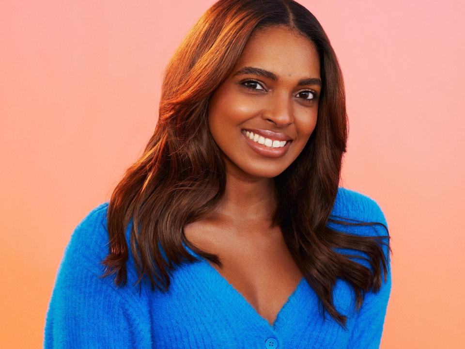 Chandler poses for photos in a blue sweater and jeans.