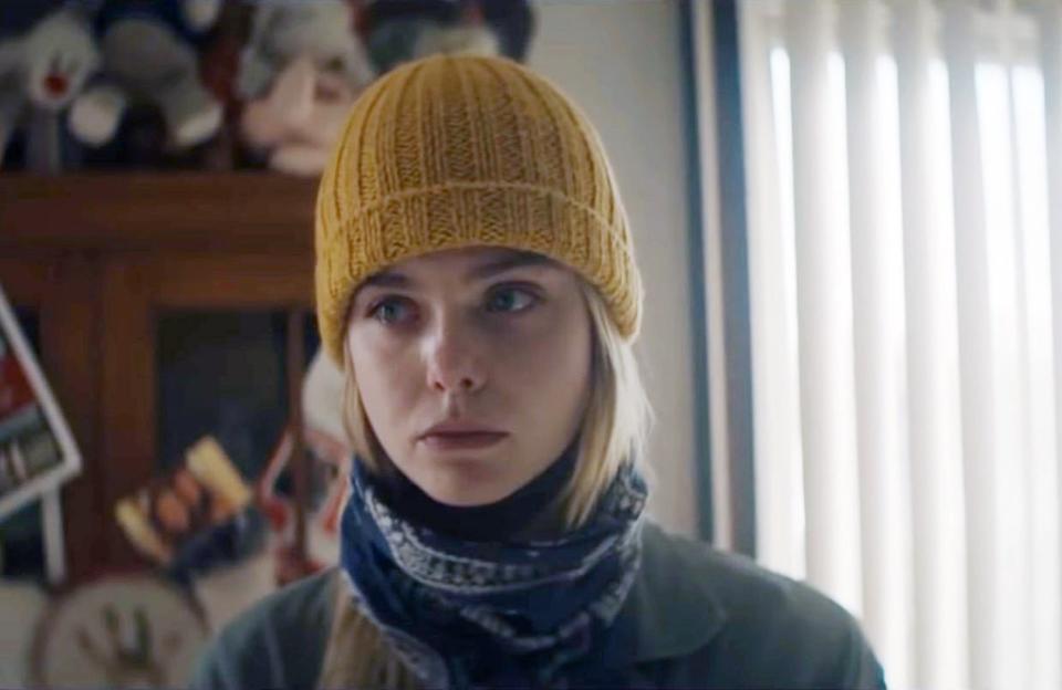 Elle Fanning stands wearing a yellow beanie, looking sad and nervous