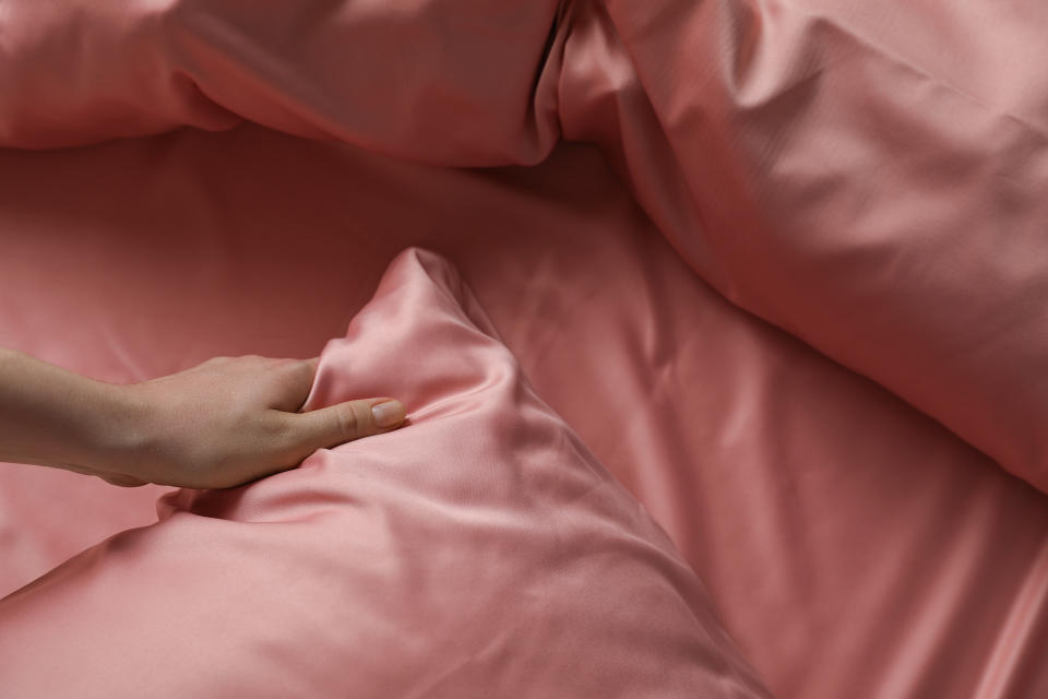 A hand feels a pink silk pillowcase, among other silk linens