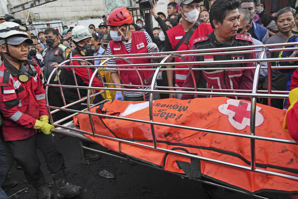 Rescuers recover the body of a victim from a neighborhood affected by a fuel depot fire in Jakarta, Indonesia, Saturday, March 4, 2023. A large fire broke out at the fuel storage depot in Indonesia's capital Friday, killing multiple people, injuring dozens of others and forcing the evacuation of thousands of nearby residents after spreading to their neighborhood, officials said. (AP Photo/Tatan Syuflana)