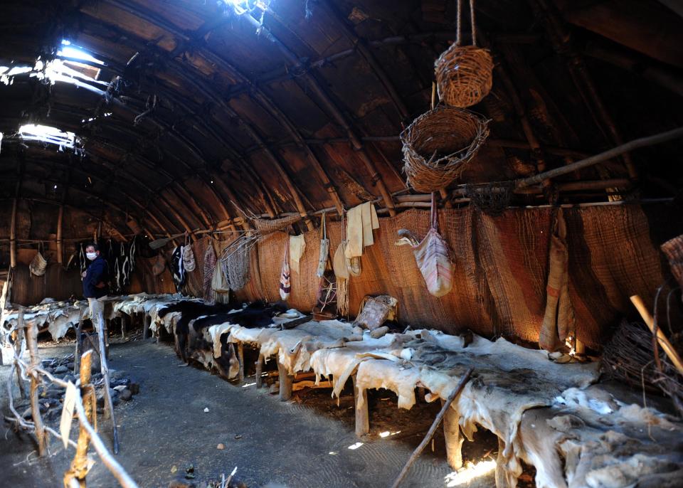 In a 2020 photograph, a Native American greeter stands in the Wampanoag winter house at Plimoth Patuxet Museums in Plymouth.