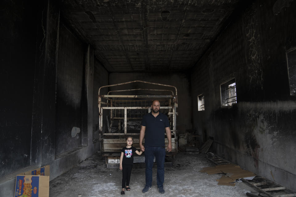 Ibrahim Dawabsha, 34, holds hands with his daughter Ghena, 3 while posing for a picture in front of his truck, at the garage of the family house, that was torched during an attack by Israel settlers last month, in the West Bank village of Duma, Tuesday, April 30, 2024. (AP Photo/Nasser Nasser)