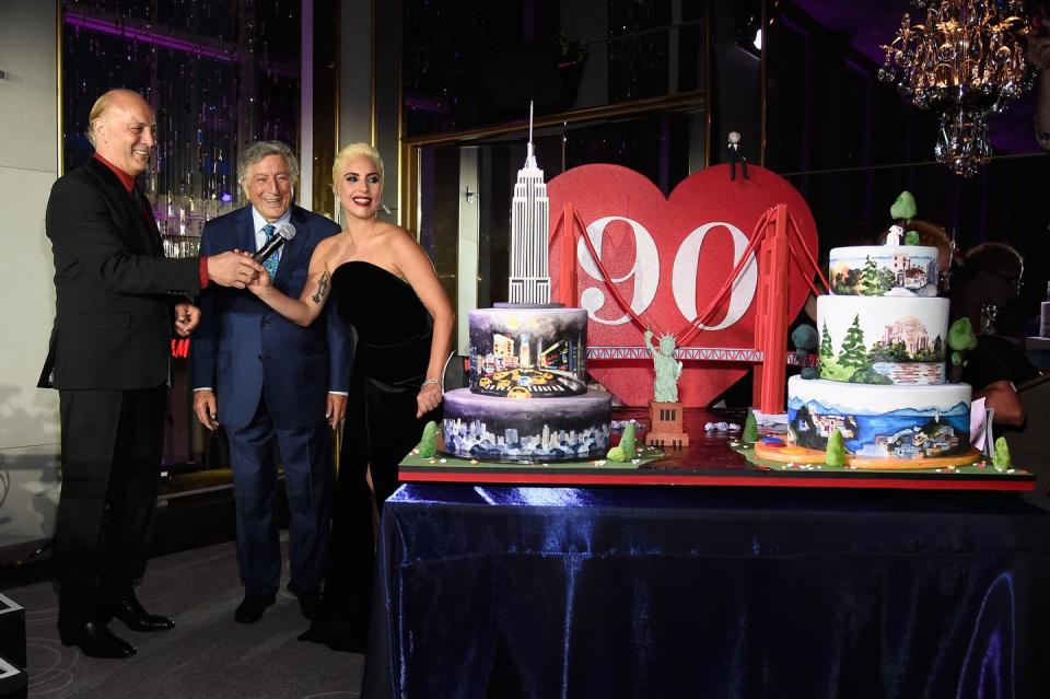 danny bennett and lady gaga hold a microphone for tony bennett as they stand next to two large cakes designed to resemble new york city