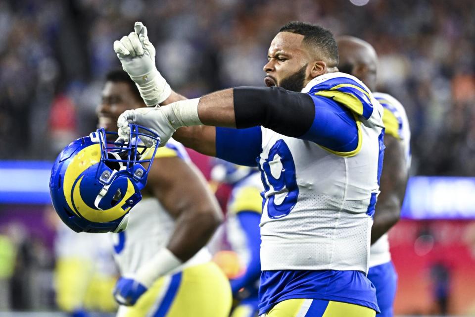 Rams defensive end Aaron Donald raises one hand while holding his helmet in his other hand.