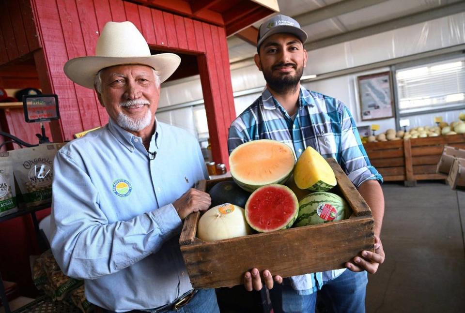 Joe Del Bosque, izquierda, con Erik Alfaro, derecha, muestran solo una pequeña selección de los melones que la familia vende en su puesto de frutas en Shields Avenue, cerca de la I-5 en el extremo oeste del Valle, el lunes 15 de julio de 2024.