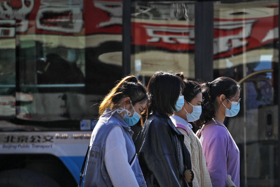 Women wearing face masks to help curb the spread of the coronavirus walk along a moving bus on a street in Beijing, Wednesday, Oct. 28, 2020. (AP Photo/Andy Wong)