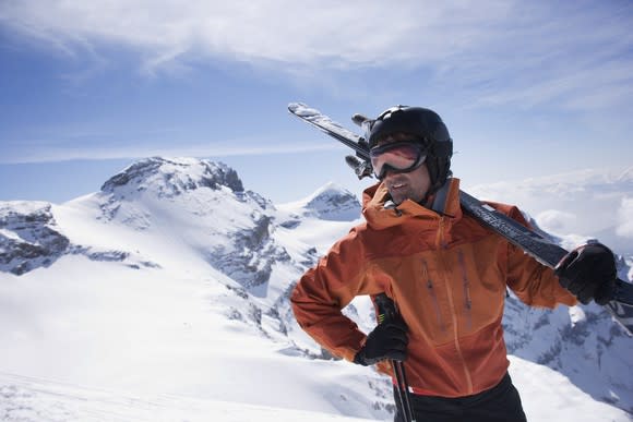 A man holding skis while looking across a snow slope.