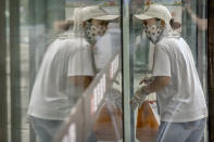 A delivery courier wearing a face mask to protect against COVID-19 is reflected in a window glass as she walks into a restaurant in Beijing, Tuesday, July 27, 2021. (AP Photo/Mark Schiefelbein)