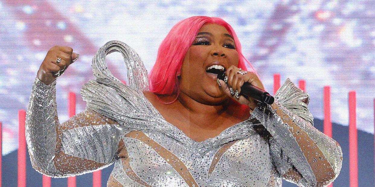 a photo of singer lizzo in a sequin jumpsuit with pink hair holding a mic on stage