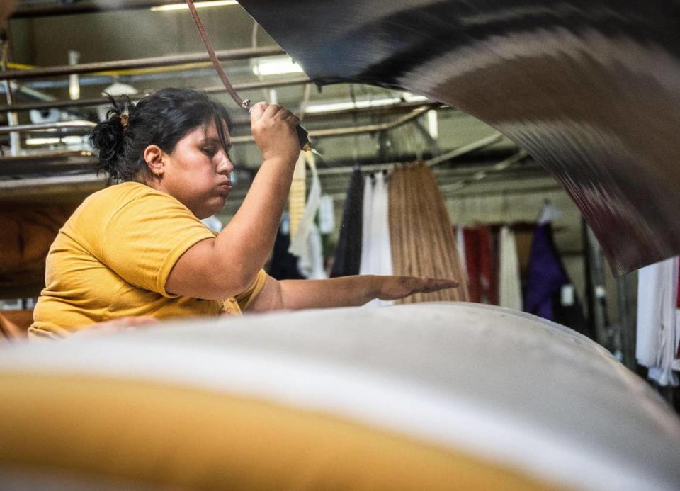 Berta Alvarado sprays water on a table cloth before ironing it at Prestige Cleaners in Sacramento on July 18, 2023.