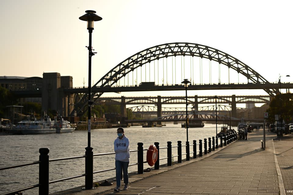 A woman wearing a protective face mask walks along the quayside, on the banks of the River Tyne, backdropped by the Tyne Bridge in Newcastle. 