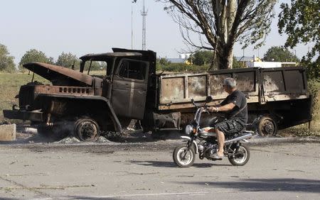 A local man rides a motorcycle past a truck burned by recent shelling on the outskirts of the southern coastal town of Mariupol September 7, 2014. REUTERS/Vasily Fedosenko