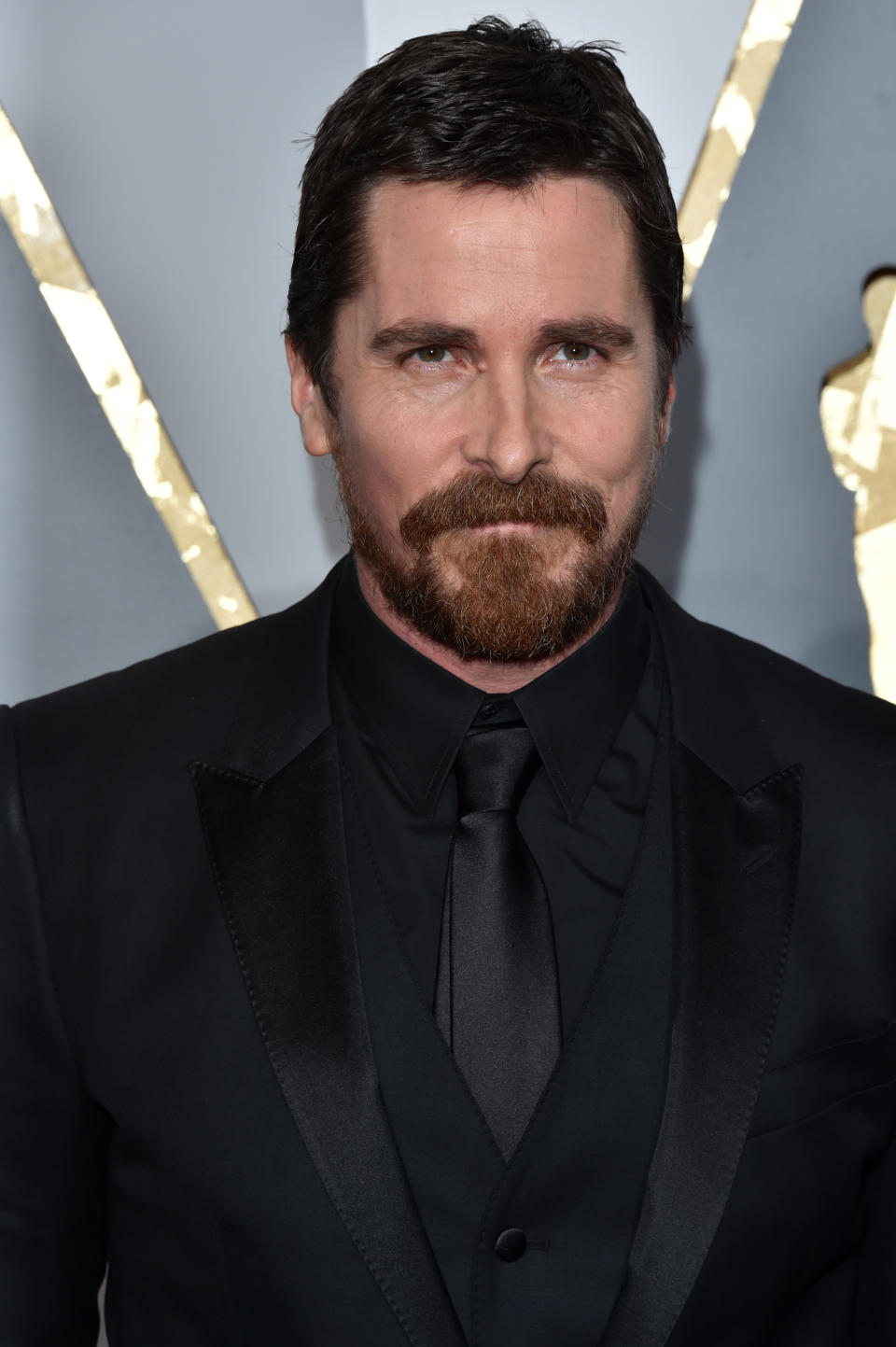 Christian Bale assistant à un événement en costume noir et cravate, avec une expression sérieuse