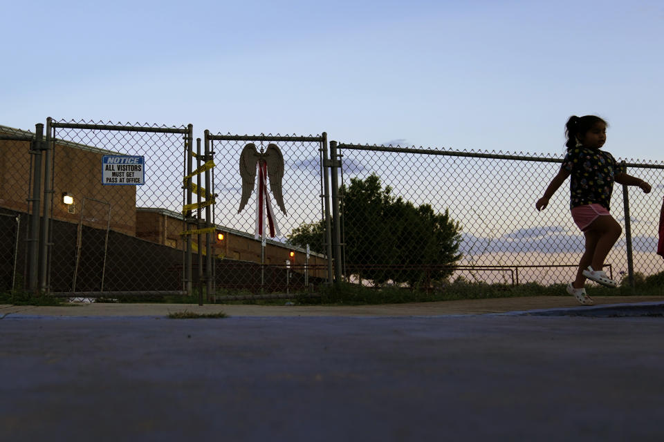 A girls skips past a gate at Robb Elementary School with police tape a locks, Sunday, July 10, 2022, in Uvalde, Texas. Students who survived the May 24 shooting at an elementary school in Uvalde, Texas are spending the summer grappling with post-traumatic stress disorder. Meanwhile, parents find themselves unable to help them, worried the tragedy at Robb Elementary struck a largely Hispanic town as Latinos continue to face disparities to access mental health care. (AP Photo/Eric Gay)