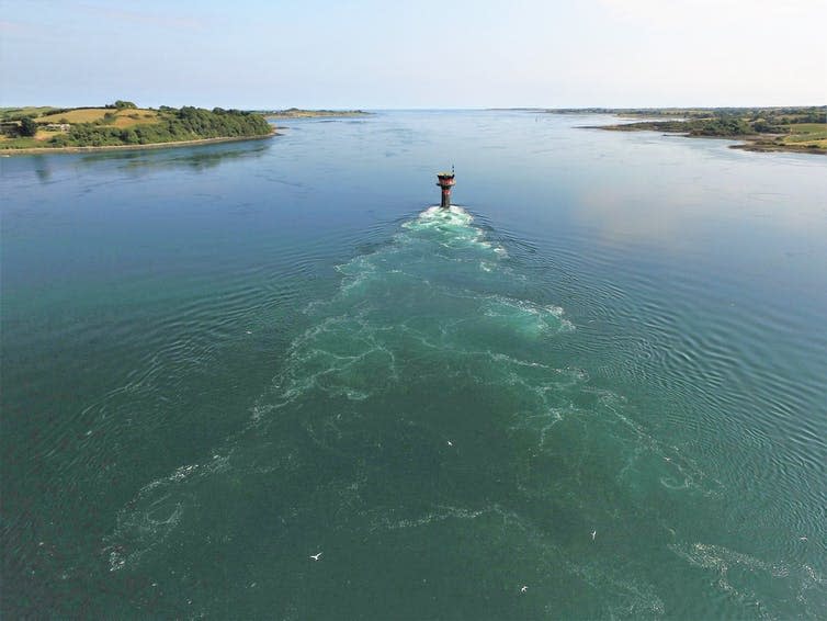 An aerial view of the sea, with turbulence caused by a human-made structure.