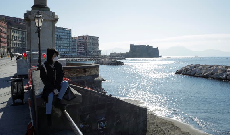 A person wearing a protective face mask sits next to the sea, after a decree orders for the whole of Italy to be on lockdown in an unprecedented clampdown aimed at beating the coronavirus, in Naples