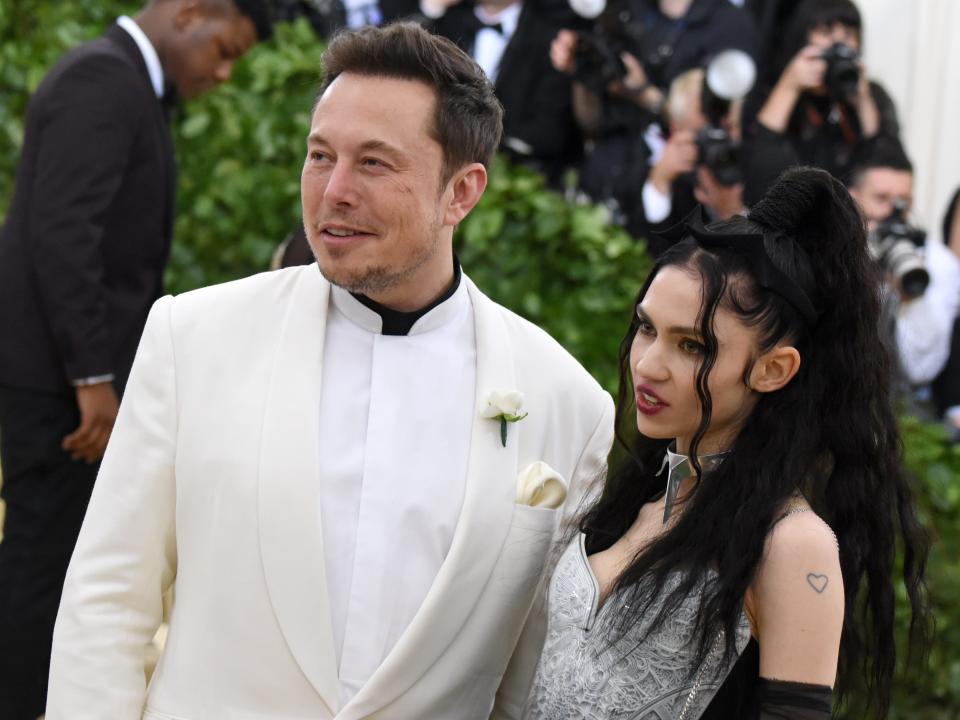 Elon Musk (left) and Grimes (right) standing next to each other and posing for photographers.