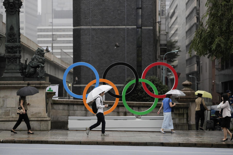 Commuters walk past the Olympic Rings Tuesday, July 23, 2019, in Tokyo. To mark the year-to-go mark, the gold, silver and bronze Olympic medals are to be unveiled Wednesday as part of daylong ceremonies around the Japanese capital. Tokyo's 1964 Olympics showcased bullet trains, futuristic designs and a new expressway, underlining Japan's recovery following World War II. Those games were the first seen worldwide by early satellites, sending the Olympics into a new era. (AP Photo/Jae C. Hong)