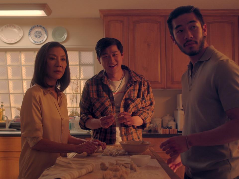 mama sun, bruce sun, and charles sun in the brothers sun, standing around a kitchen island making dumplings