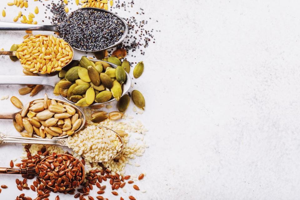 seeds of pumpkin, flax, sesame, sunflower and poppy in metal spoons in the left part of a table with the copy of space, the top view