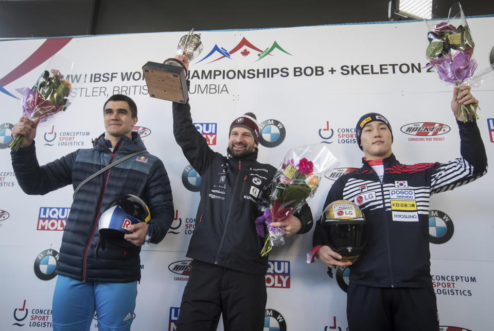 Martins Dukurs, center, of Latvia, holds up the trophy after winning the men's event while posing with Russia's Nikita Tregubov, left, who finished second, and South Korea's Sungbin Yun, who finished third, at the Skeleton World Championships in Whistler, British Columbia, Friday March 8, 2019. (Darryl Dyck/The Canadian Press via AP)