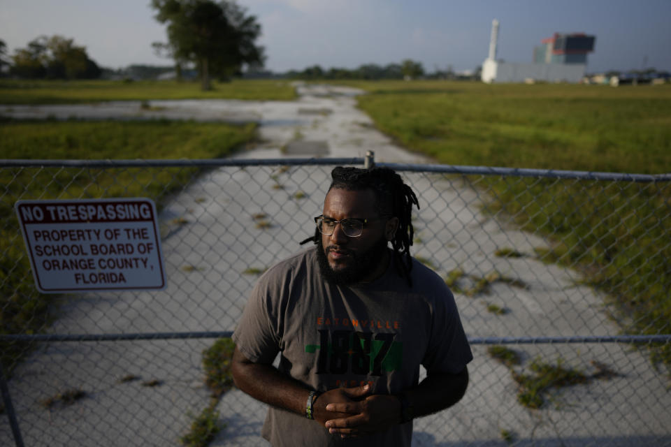 Julian Johnson, 30, who founded the 1887 First organization to protect the property where Robert Hungerford Normal and Industrial School once stood, poses for a picture in front of the closed former school grounds in the heart of Eatonville, Fla., Thursday, Aug. 24, 2023. Named for the year that Eatonville was incorporated as a self-governing Black municipality, the organization has since broadened its mission to include both historic preservation and community strengthening. (AP Photo/Rebecca Blackwell)