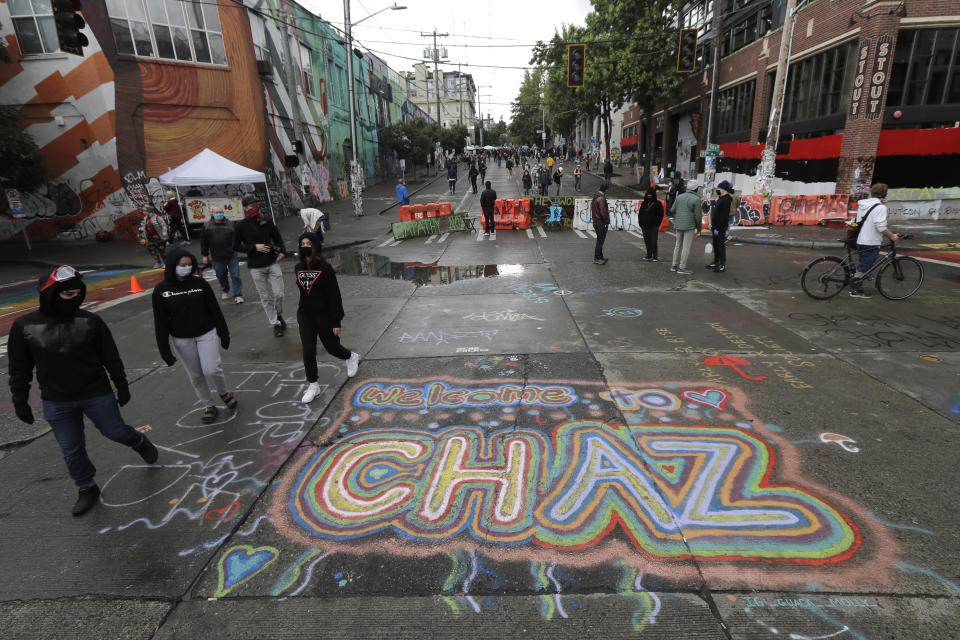 FILE - In this Thursday, June 11, 2020 file photo, people walk past street art that reads "Welcome to CHAZ" inside what is being called the "Capitol Hill Autonomous Zone" in Seattle. On Friday, June 19, 2020, The Associated Press reported on a manipulated image circulating online incorrectly depicting residents of Seattle’s occupied protest zone planting their new official flag, which has a pink unicorn and the acronym “CHAZ” on it, in an overflowing trash can. The original version of the manipulated photo was posted in 2017, and does not show a unicorn or the acronym “CHAZ” on the flag. There is no evidence that protesters in the Capitol Hill neighborhood have chosen any official flag. (AP Photo/Ted S. Warren)