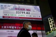 A man wearing a face mask walks past a bank's electronic board showing the Hong Kong share index in Hong Kong, Thursday, Dec. 2, 2021. Asian stock markets were mixed Thursday after a turbulent day on Wall Street as traders tried to forecast the impact of the coronavirus's omicron variant. (AP Photo/Kin Cheung)