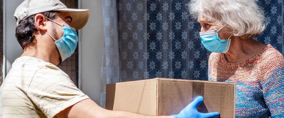 Young male volunteer in mask gives an elderly woman boxes