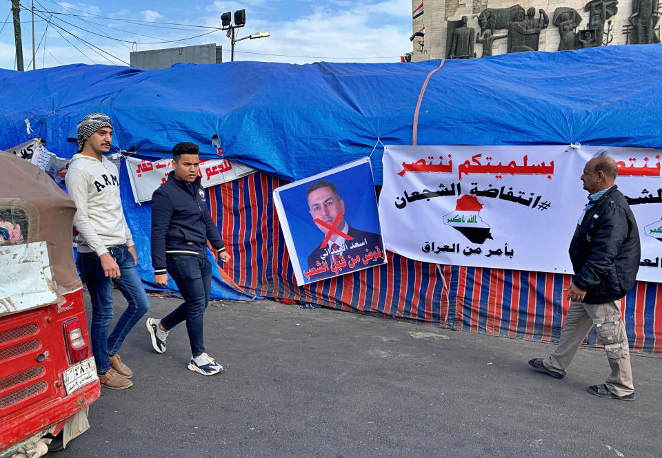 Anti-government protesters walk past a poster with a defaced picture of the governor of the southern Basra province Asaad al-Eidani and Arabic that reads "rejected by the people," during the ongoing protests, in Tahrir square, in Baghdad, Iraq, Wednesday, Dec. 25, 2019. An Iranian-backed bloc in Iraq's parliament proposed al-Eidani as the country's next prime minister. However, the nomination was promptly rejected by Iraqi protesters who want an independent candidate to take over the government. Earlier on Wednesday, outgoing higher education minister, who had also been rejected by protesters on the streets, withdrew his nomination for prime minister. (AP Photo/Ali Abdul Hassan)