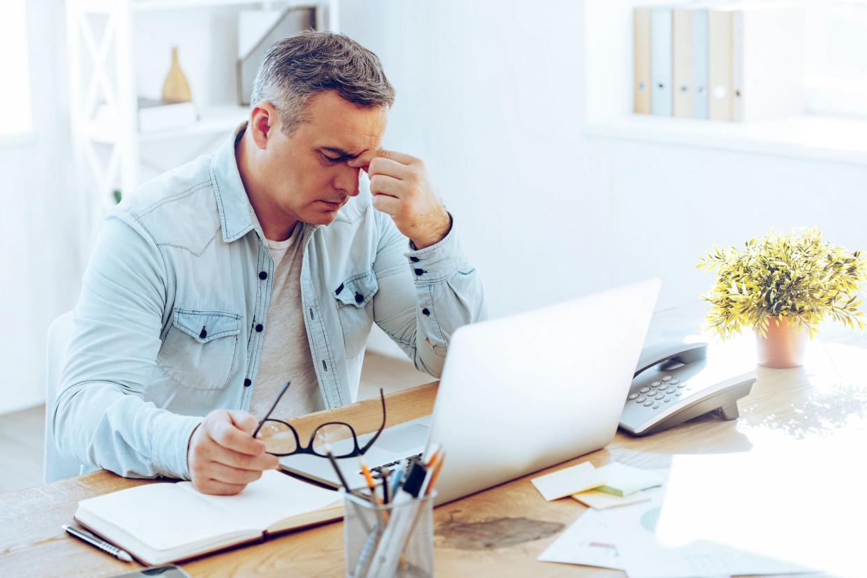 frustrated middle-aged man at computer with papers on desk